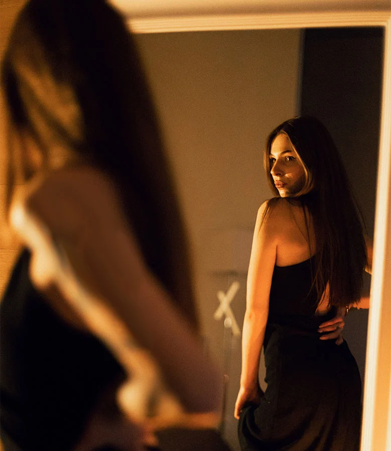 woman looking in the mirror in a dark room | Arslanian Plastic Surgery Atlanta